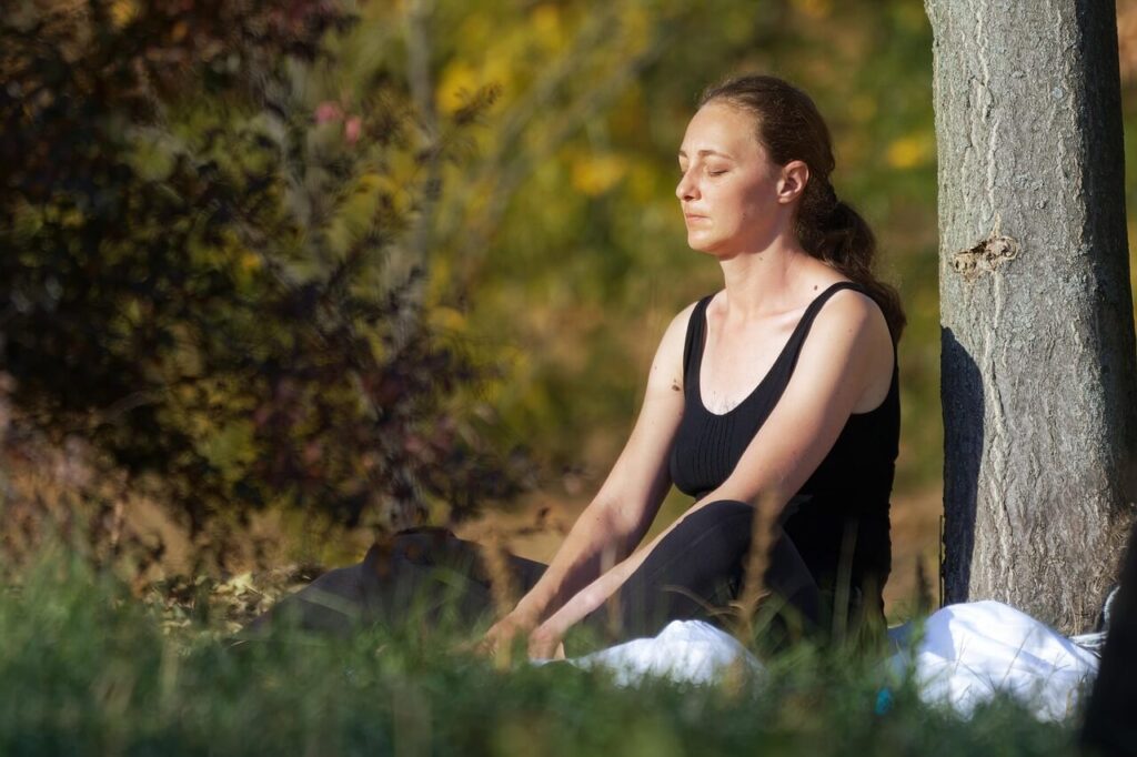 Woman in meditative pose outdoors practicing mindfulness and stress relief.